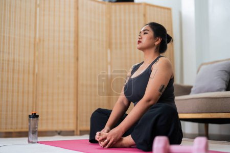 Foto de Mujer asiática con sobrepeso haciendo ejercicio de estiramiento en casa en forma física, ejercicio de entrenamiento de estiramiento en estera de yoga en casa para una buena salud y forma del cuerpo. - Imagen libre de derechos