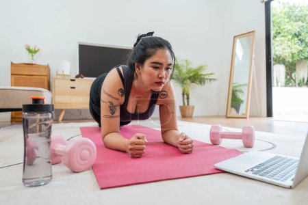 Téléchargez les photos : Asiatique femme en surpoids faisant des exercices d'étirement à la maison sur la forme physique, cours de conditionnement physique en ligne. Entraînement d'étirement sur tapis de yoga à la maison pour une bonne santé et forme du corps. - en image libre de droit