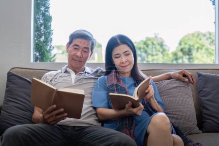 Photo for Happy elderly couple relax on couch in living room reading together for vacation holiday at home. - Royalty Free Image