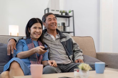 Foto de Asiático senior pareja disfrutando en su favorito TV. Feliz pareja de jubilados viendo televisión juntos en la sala de estar. - Imagen libre de derechos