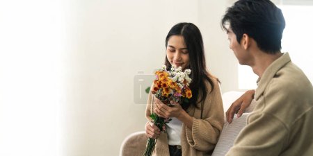 Foto de Asiático guapo hombre mostrar el amor y dar flores a su novia en sala de estar en día de San Valentín. Concepto de estilo de vida. - Imagen libre de derechos