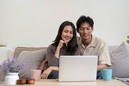 Téléchargez les photos : Jeune couple asiatique en utilisant ordinateur portable ensemble tout en étant assis sur le canapé à la maison. - en image libre de droit