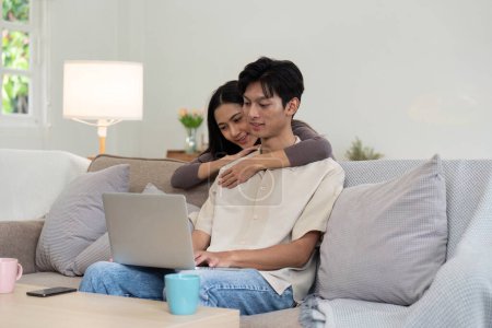 Photo for Young couple asian using laptop together while sitting on sofa at home. - Royalty Free Image
