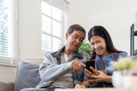 Foto de Retrato de asiático adorable pareja de personas mayores utilizando el teléfono inteligente juntos video chat con la familia en la sala de estar en casa.. - Imagen libre de derechos