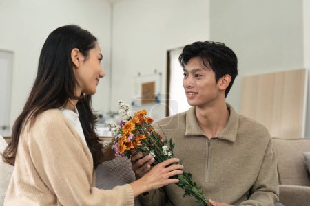 Téléchargez les photos : Asiatique bel homme montrer l'amour et donner des fleurs à sa petite amie dans le salon le jour de la Saint-Valentin. Concept de style de vie. - en image libre de droit