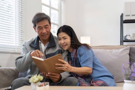 Photo for Asian senior couple reading book diary together, sitting on cozy sofa in home interior. Happy retirement activity lifestyle at home. - Royalty Free Image