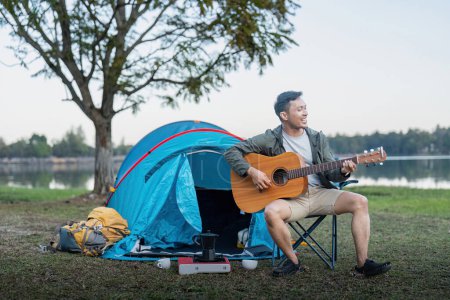 Téléchargez les photos : Homme asiatique voyager avec tente camping sur montagne en plein air aventure style de vie randonnée actif vacances d'été tout en jouant de la guitare. - en image libre de droit