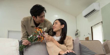 Téléchargez les photos : Romantique jeune couple asiatique embrassant avec tenant des fleurs et souriant dans le salon à la maison. tomber amoureux. Concept de Valentin. - en image libre de droit