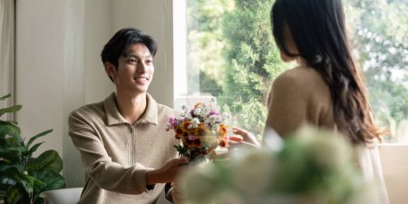Photo for Romantic young asian couple embracing with holding flowers and smiling in living room at home. fall in love. Valentine concept. - Royalty Free Image