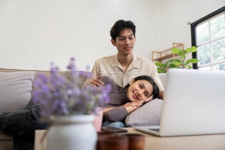 Téléchargez les photos : Heureux couple asiatique asseoir relax sur canapé dans salon regarder vidéo sur portable ensemble à la maison. - en image libre de droit