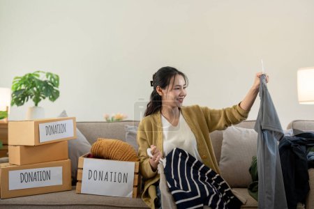 Téléchargez les photos : Femme asiatique tenant boîte de don pleine de vêtements et de certains vêtements. Concept de don et de recyclage des vêtements. Aider les pauvres. - en image libre de droit