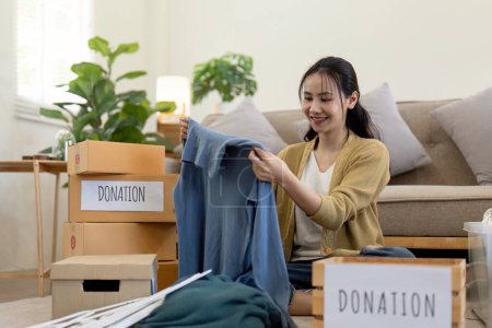Mujer asiática sosteniendo caja de donación llena de ropa y ropa selecta. Concepto de donación y reciclaje de ropa. Ayudar a los pobres.