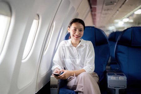 Photo for Successful asian businesswoman or female entrepreneur in a plane sits in a business class seat. - Royalty Free Image