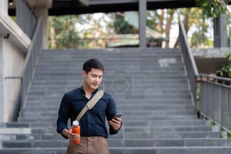 Foto de Sonriente asiático hombre de negocios caminando al trabajo, mientras que para mantener reutilizable eco amigable copa ecológica en la ciudad. - Imagen libre de derechos