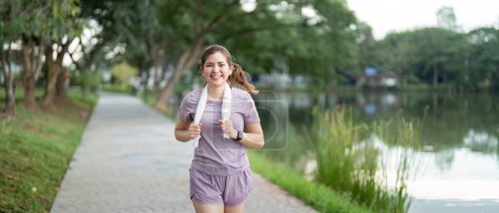 Téléchargez les photos : Femme active femme asiatique en vêtements de sport écouter de la musique tout en courant ou en faisant du jogging dans le parc le matin. - en image libre de droit