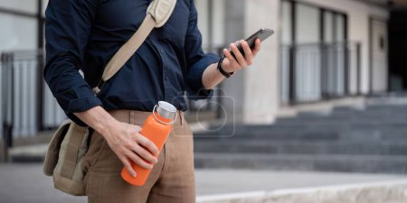 Téléchargez les photos : Homme d'affaires marchant au travail tout en tenant une tasse écologique réutilisable dans la ville. - en image libre de droit
