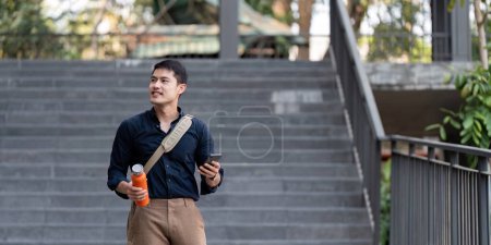 Photo for Smiling asian businessman walking to work while to hold reusable eco friendly ecological cup in the city. - Royalty Free Image