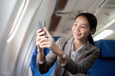Téléchargez les photos : Femme d'affaires asiatique est assis dans l'avion et en utilisant un téléphone portable pendant le voyage ou aller au travail. - en image libre de droit