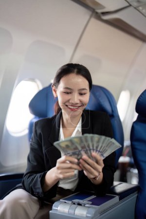 Foto de Joven mujer de negocios exitosa con dinero en la mano y en el avión sentado. - Imagen libre de derechos