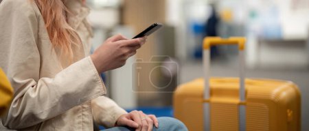 Foto de Mujer turista usando smartphone móvil con maleta que viaja entre esperas para el vuelo en la terminal del aeropuerto, check in de vuelo, concepto de viaje turístico. - Imagen libre de derechos