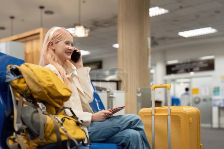 Foto de Mujer turista asiática feliz usando teléfono inteligente móvil con maleta de viaje entre espera de vuelo en la terminal del aeropuerto, check in de vuelo, concepto de viaje turístico. - Imagen libre de derechos