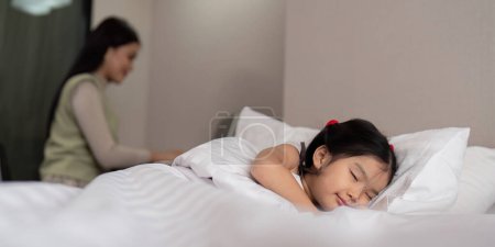 Photo for Asian mother working on bed with sleeping daughter by side at home. - Royalty Free Image