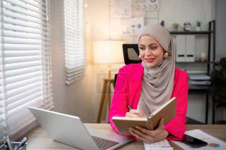 Téléchargez les photos : Femme musulmane asiatique d'affaires utilisant la calculatrice et l'écriture prendre note avec calculer la finance sur un bureau. Femme travaillant au bureau avec ordinateur portable et impôts, comptabilité, documents sur le bureau. - en image libre de droit
