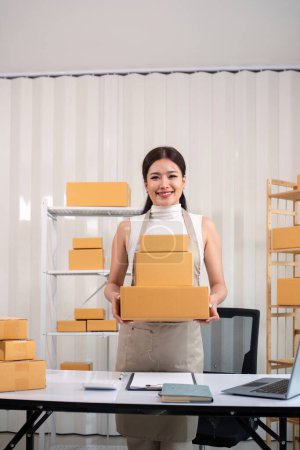 Foto de Joven mujer de negocios asiática trabajando en línea ecommerce compras en su tienda. Mujer joven vende preparar caja de paquete de producto para entregar al cliente. Venta en línea. - Imagen libre de derechos