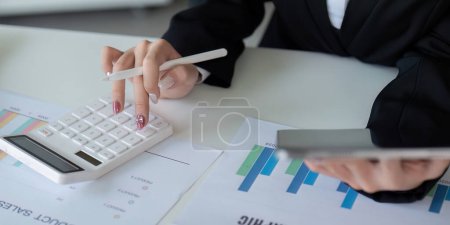 Photo for Finance concept. Close up businesswoman hold a graph pen and writing report, and memo, and analyzing business documents with a laptop computer. - Royalty Free Image