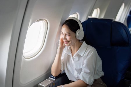 Photo for Asian young woman wearing headphone listen to music at first class on airplane during flight, Traveling and Business concept. - Royalty Free Image