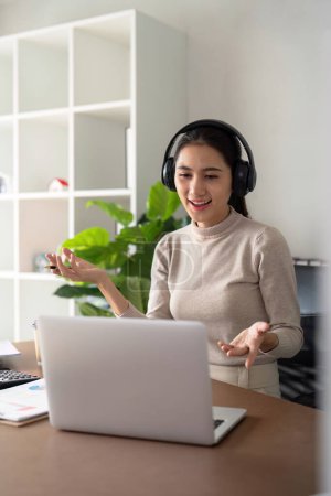Téléchargez les photos : Femme asiatique sur appel vidéo avec le travail à partir d'un ordinateur portable à la maison, écouteurs et réunion virtuelle internationale en ligne. Webinaire pour le travail à distance ou la mise à jour globale sur ordinateur. - en image libre de droit