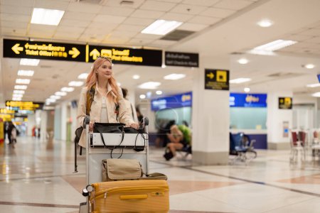 Foto de Feliz mujer turista asiática con mochila y equipaje viajando entre esperas para el vuelo en la terminal del aeropuerto, concepto de viaje turístico. - Imagen libre de derechos