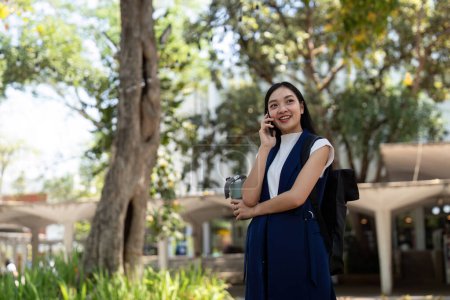 Foto de Joven feliz asiático negocios mujer oficina profesional hablar celular en caminar en la ciudad ir a trabajar. - Imagen libre de derechos