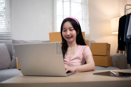 Téléchargez les photos : Heureux jeune propriétaire d'entreprise asiatique femme préparer boîte de colis et vérifier la commande en ligne de produit pour livrer au client sur ordinateur portable. Shopping Concept en ligne. - en image libre de droit