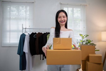 Téléchargez les photos : Heureuse jeune femme asiatique démarrage petite entreprise freelance tenant boîte de colis. Concept de livraison de boîte d'emballage marketing en ligne. - en image libre de droit