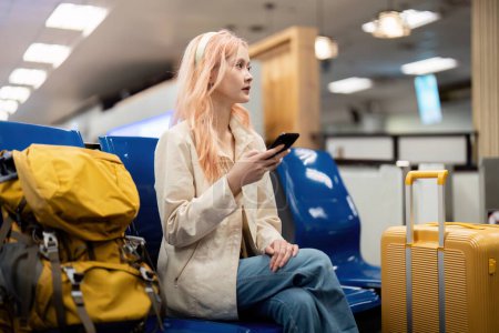 Foto de Mujer turista asiática feliz usando teléfono inteligente móvil con maleta de viaje entre espera de vuelo en la terminal del aeropuerto, check in de vuelo, concepto de viaje turístico. - Imagen libre de derechos