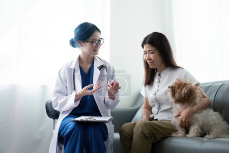 Téléchargez les photos : Femme âgée avec chien assis par bureau devant une femme vétérinaire asiatique à la clinique vétérinaire. - en image libre de droit