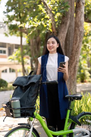 Photo for Asian businesswoman with bicycle using smartphone and outside the office building. Woman commuting on bike go to work. Eco friendly vehicle, sustainable lifestyle concept. - Royalty Free Image