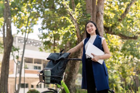 Téléchargez les photos : Femme d'affaires asiatique avec vélo tenant un ordinateur portable et à l'extérieur de l'immeuble de bureaux. Les femmes qui font la navette à vélo vont au travail. Véhicule écologique, concept de mode de vie durable. - en image libre de droit