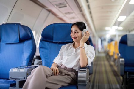 Foto de Mujer joven asiática con auriculares escuchar música en primera clase en el avión durante el vuelo, Viajar y concepto de negocios. - Imagen libre de derechos