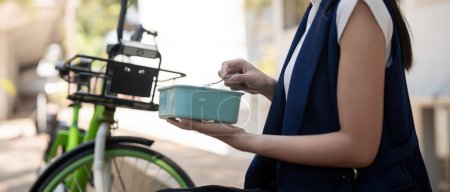 Jungunternehmerin beim Essen einer Lunchbox, die während der Arbeitspause auf einer Treppe sitzt, Konzept gesunder Ernährung mit dem Fahrrad zum Autofahren, umweltfreundliches Fahrzeug, nachhaltiges Lifestylekonzept.