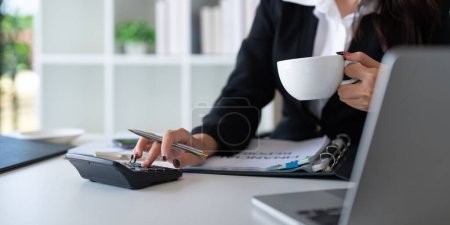 Téléchargez les photos : Femme d'affaires comptable à l'aide d'une calculatrice et d'un ordinateur portable pour l'épargne de données financières dans la salle de bureau, Financière d'entreprise, fiscalité, concept comptable. - en image libre de droit
