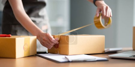 Photo for Woman use scotch tape to attach parcel box to prepare goods for the process of packaging, shipping, online sale internet marketing ecommerce concept startup business idea. - Royalty Free Image