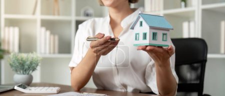 Hausverkauf und Hausversicherungs-Konzept, Immobilienmakler mit Hausmodell im Gespräch mit dem Kunden über den Kauf von Hausversicherungen und Unterzeichnung des Vertrages unter formeller Vertragsvereinbarung.