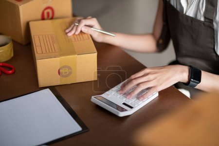 Photo for Woman entrepreneur prepare parcel box and check online order on laptop computer for commercial checking delivery. online marketing, packing box, SME seller. startup business concept. - Royalty Free Image
