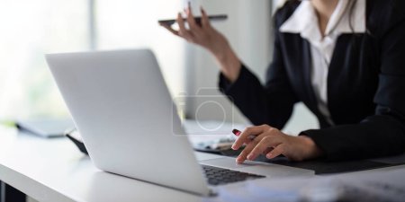 Téléchargez les photos : Femme d'affaires travaillant à l'aide d'un ordinateur portable pour enregistrer et imprimer des informations pour un plan de marketing analyser le rapport de bilan états financiers. - en image libre de droit