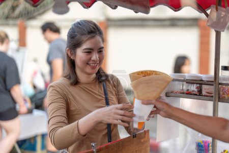 Fröhliche junge asiatische Reisende Feinschmeckerfrau bestellt Crepes bei Streetfood-Verkäufer auf dem Nachtmarkt im Freien.