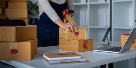 Photo for Woman use scotch tape to attach parcel box to prepare goods for the process of packaging, shipping, online sale internet marketing ecommerce concept startup business idea. - Royalty Free Image