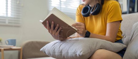Foto de Mujer joven sentada en un sofá y leyendo un libro disfruta del descanso. relajarse en casa. - Imagen libre de derechos