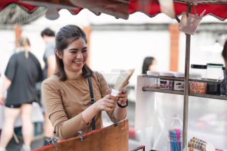 Téléchargez les photos : Heureux jeune asiatique voyageur foodie femme commander crêpes en plein air nuit marché rue nourriture vendeur. - en image libre de droit
